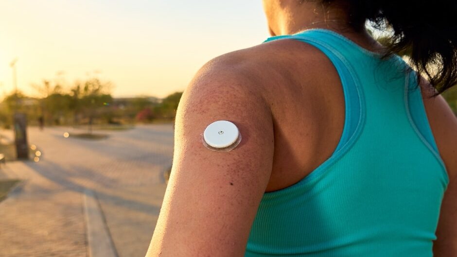 Female runner wearing a continuous glucose monitor sensor on her upper arm while outdoors at sunset